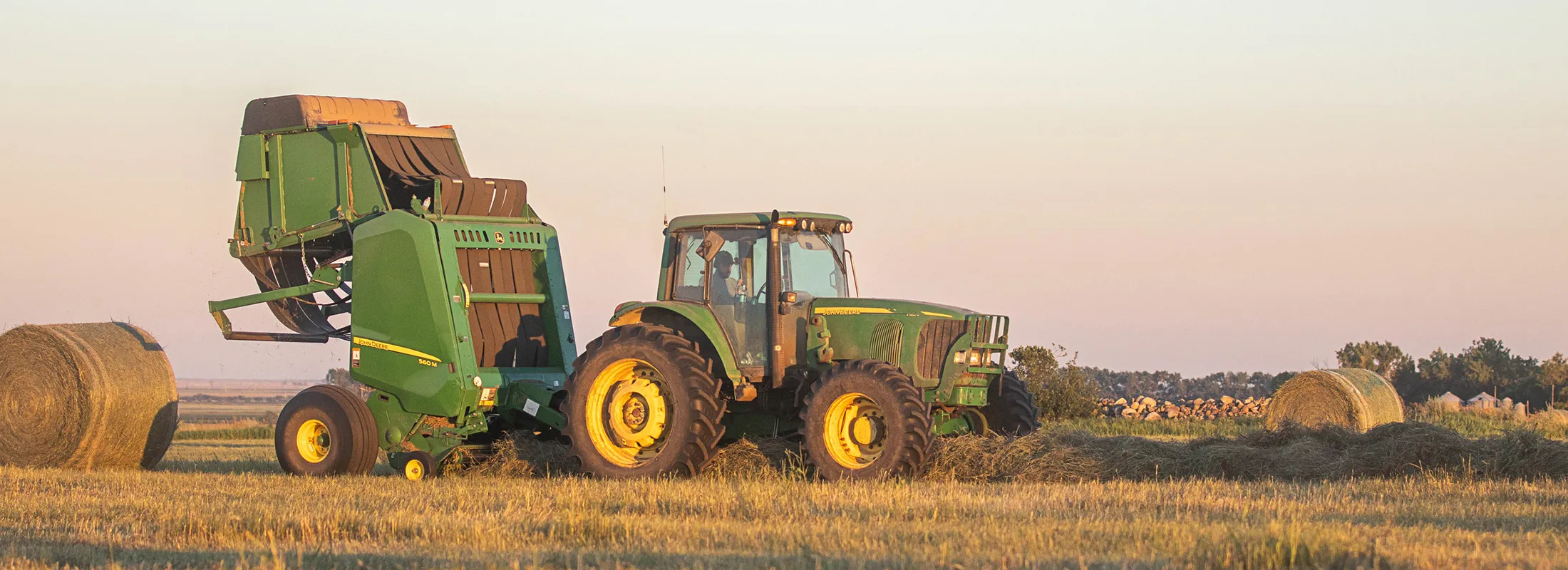 a tractor pulling a baler in a field with hay bales