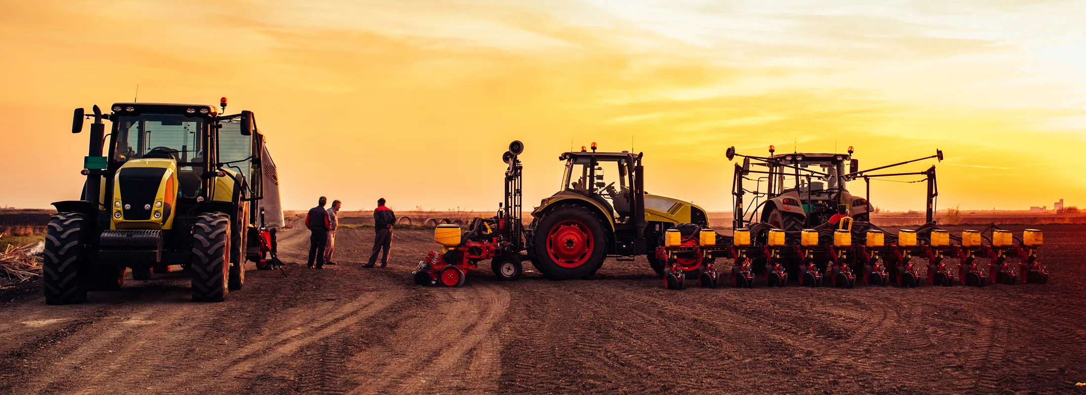 two large tractors each connected to a planter with a group of men talking nearby 