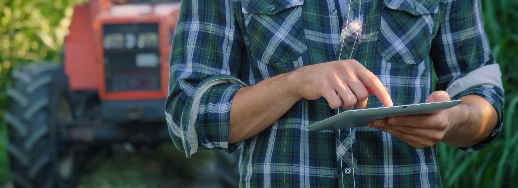 a man working on a tablet with a tractor in the background