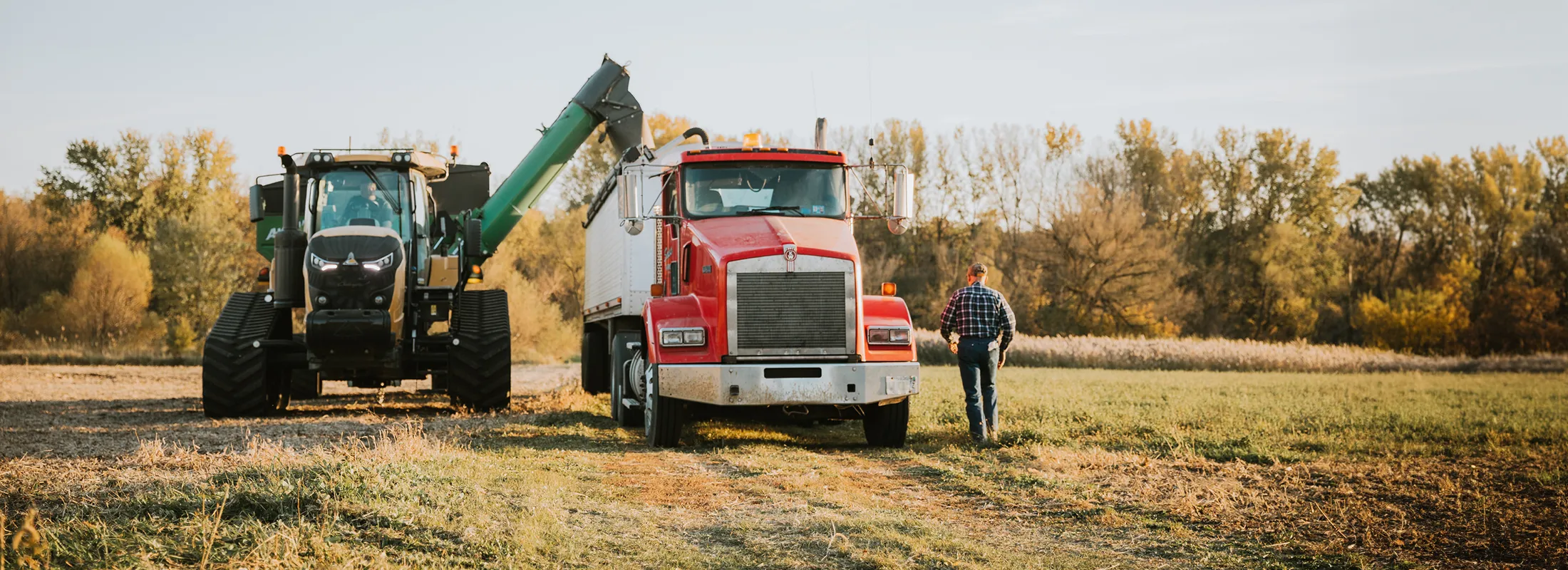 a tractor using an auger to transfer material into an open truck with a person standing nearby
